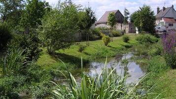 Un paysage paisible au bord de la rivière, avec une végétation luxuriante et des bâtiments traditionnels en pierre.