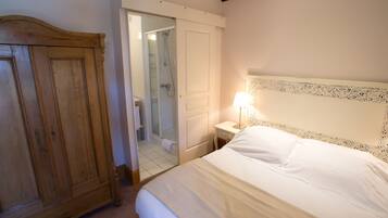 A bedroom with a wooden wardrobe, a bedside table with a lamp, and a bathroom visible through an open door.
