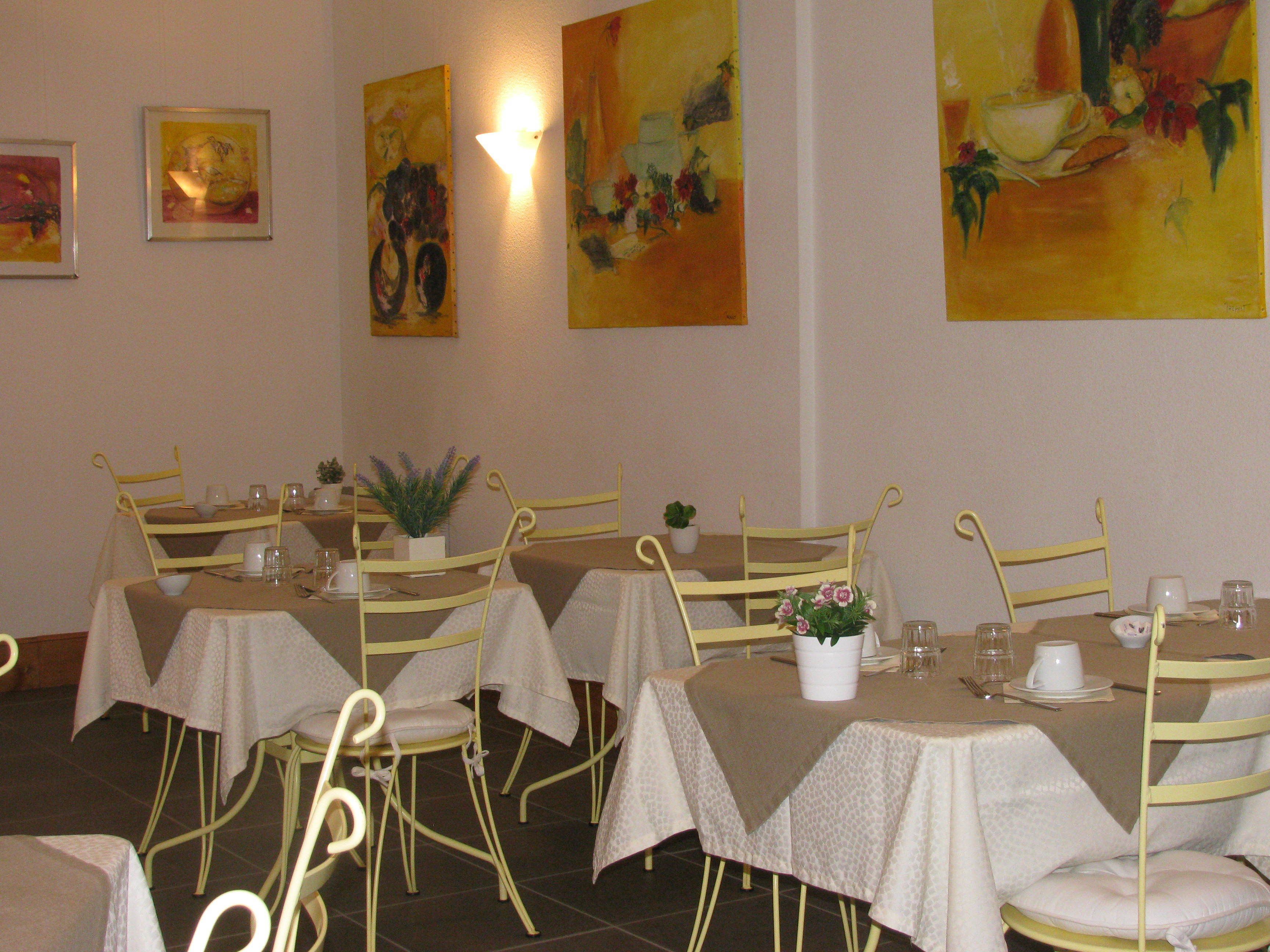 Un comedor con mesas y sillas, obras de arte en las paredes y una planta en maceta sobre las mesas.