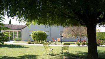 A building with a white exterior, a paved driveway, and a well-maintained lawn. There are two lawn chairs under a tree.