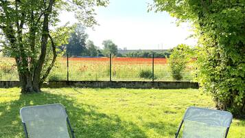 Two foldable chairs with a small round table in a grassy outdoor area with trees and a fence in the background.