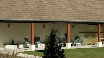 Un'area salotto esterna coperta con sedie e tavoli, un tetto piastrellato e un piccolo albero sullo sfondo.