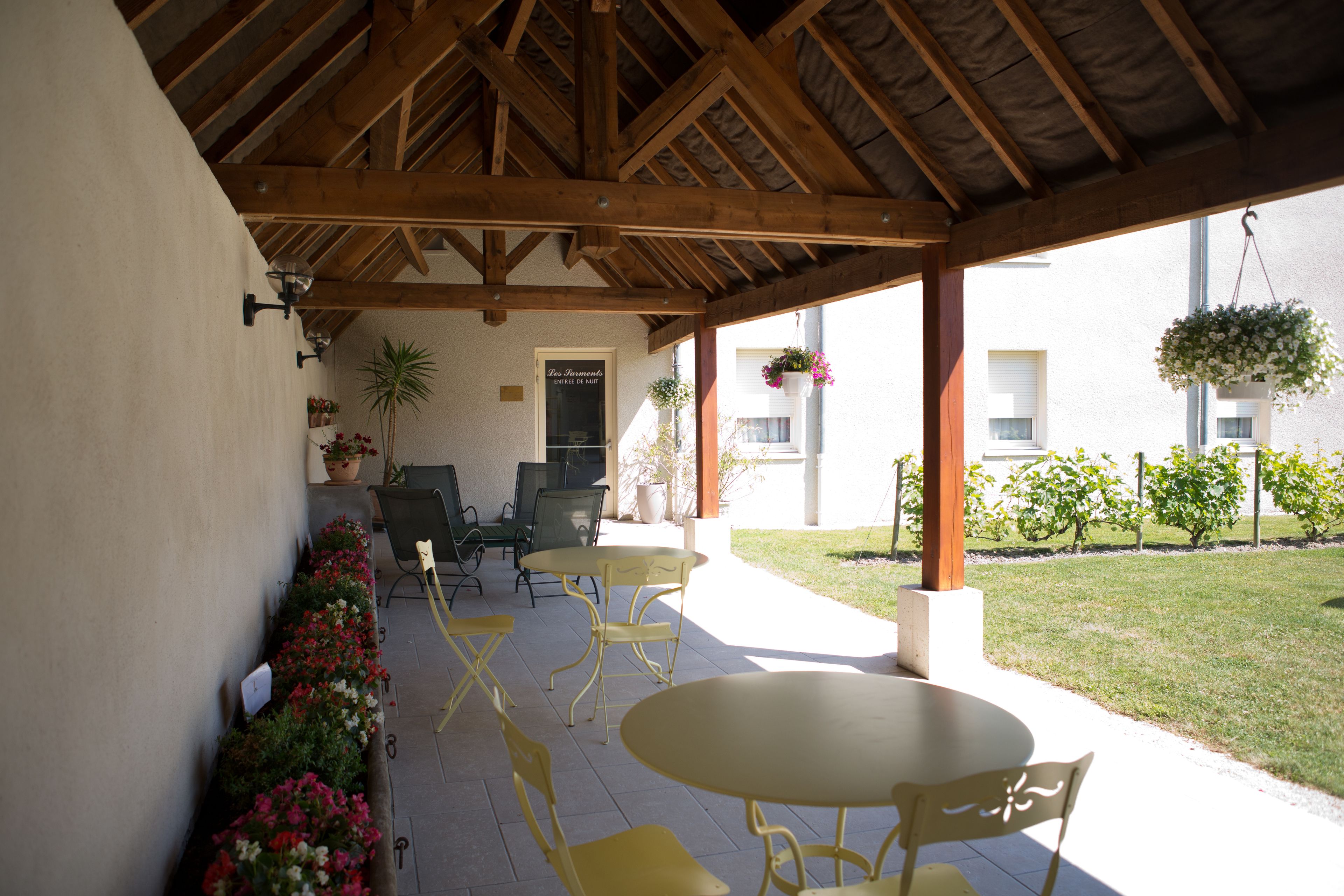 A covered patio with yellow chairs and a table, surrounded by potted plants and a small garden.