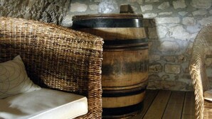 Una habitación rústica con un sofá de mimbre, un barril de madera y paredes de piedra.