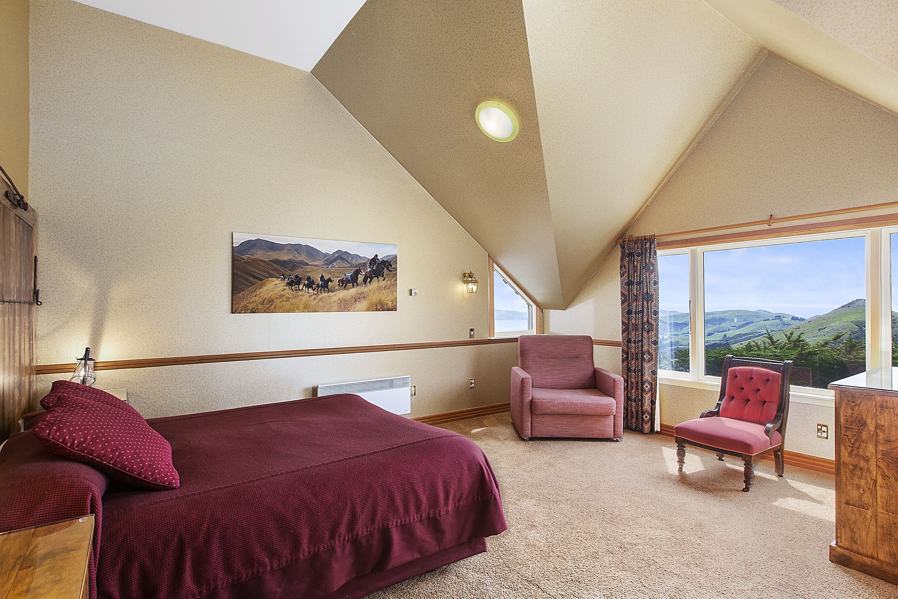 A bedroom with a large bed, a chair, and a window with a view of hills.