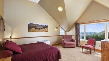 A bedroom with a large bed, a chair, and a window with a view of hills.