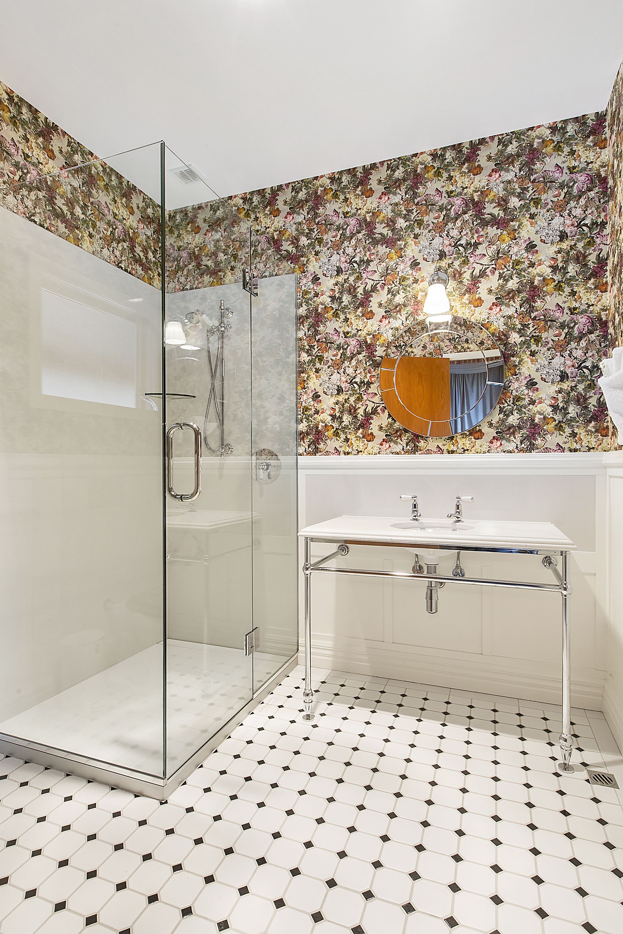 A bathroom with a glass-enclosed shower, a white sink with chrome fixtures, and a floral-patterned wall.
