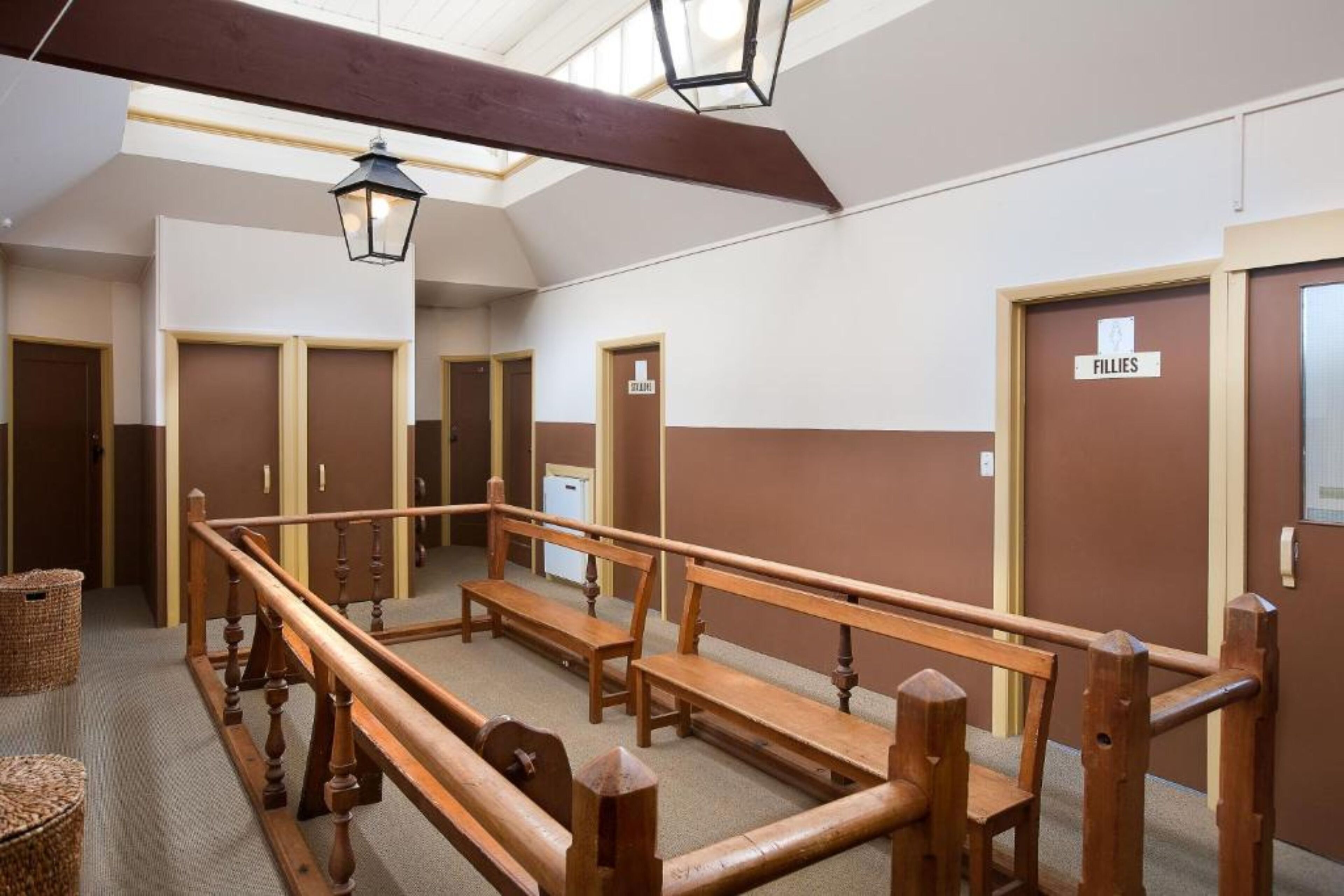 A hotel lobby with wooden benches, a high ceiling with skylights, and doors labeled "FILLIES".