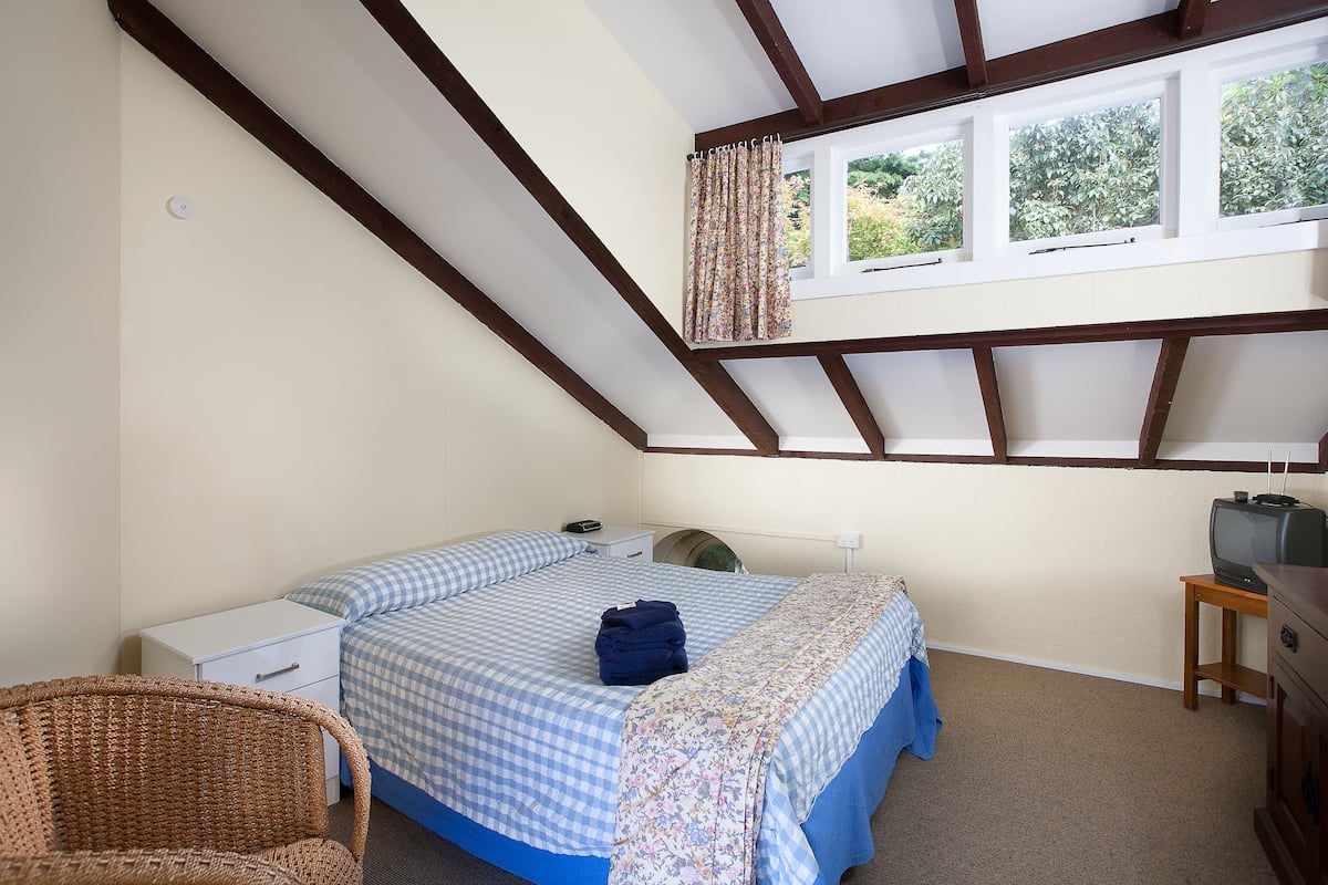 A bedroom with a bed, a chair, a TV, and a window with curtains.