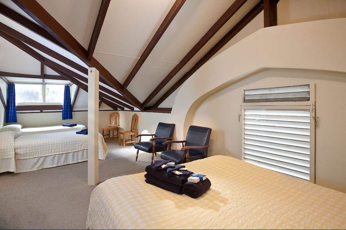 A room with two beds, a desk, and a window with blinds.