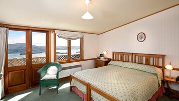 A bedroom with a large bed, a chair, a nightstand, a lamp, and a view of the outdoors.