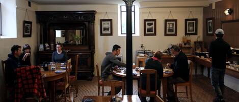 A restaurant with wooden tables and chairs, exit signs, framed pictures on the walls, and a brick floor.