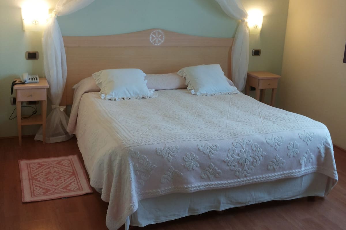 A bedroom with a canopy bed, two bedside tables, a nightstand, and a decorative rug.