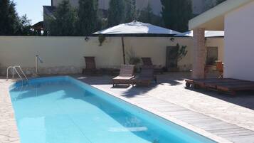Ein rechteckiger Pool mit Holzterrasse, umgeben von Liegestühlen und Sonnenschirmen.