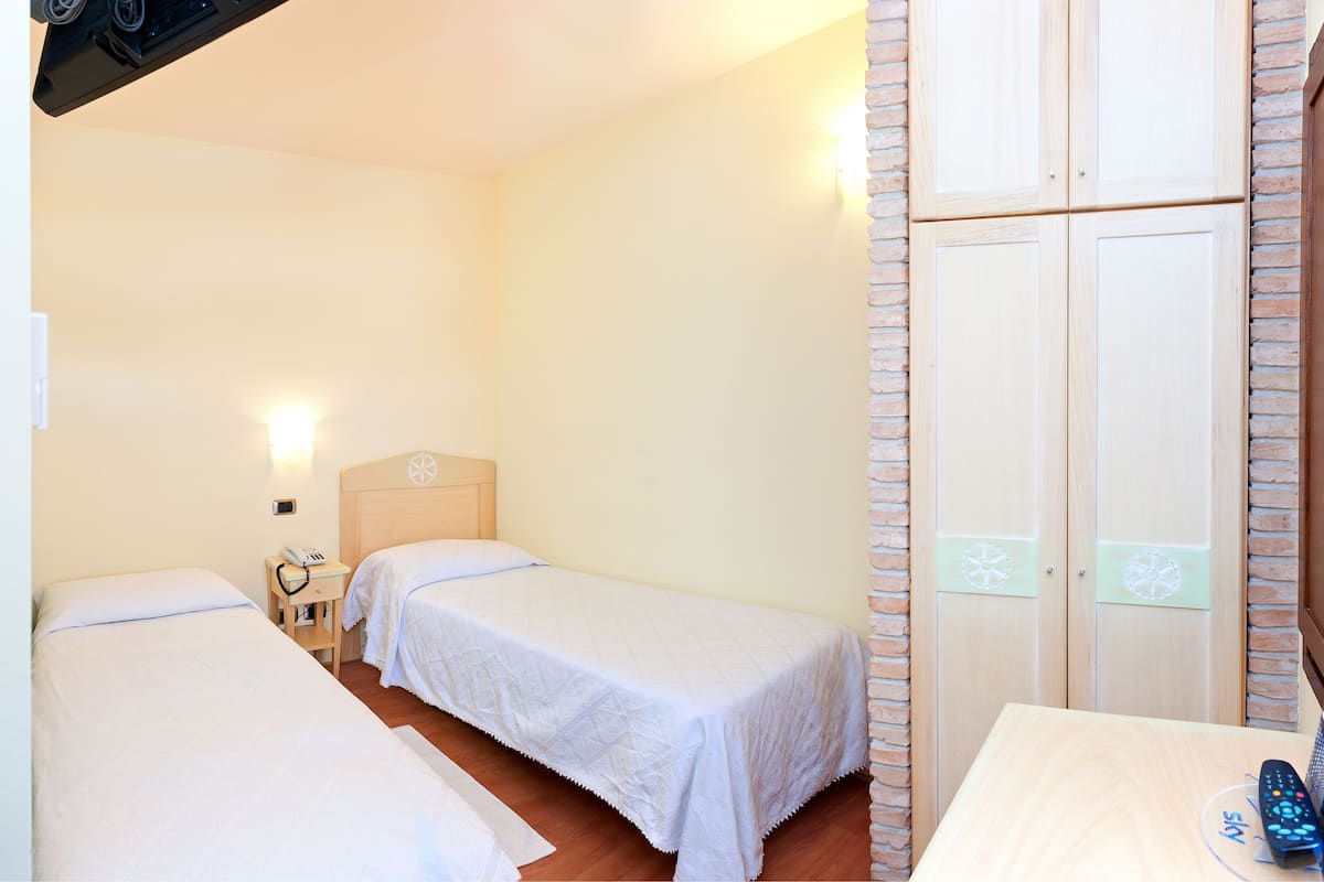 A hotel room with two single beds, a wooden nightstand with a phone, a small table with a remote control, and a brick-patterned wardrobe.