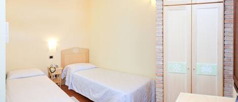 A hotel room with two single beds, a wooden nightstand with a phone, a small table with a remote control, and a brick-patterned wardrobe.