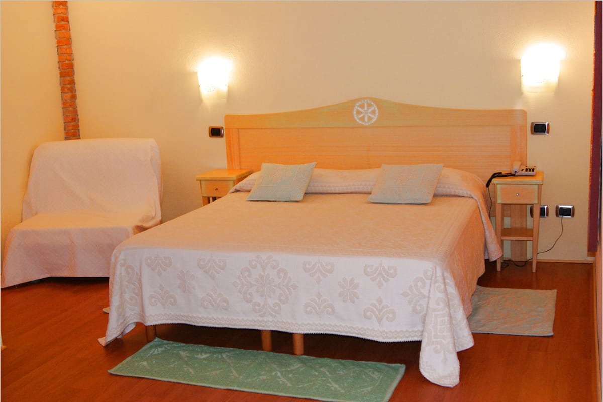 A bedroom with a wooden bed, two bedside tables, a nightstand, a green rug, and a chair.