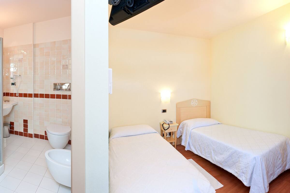 A hotel room with a shower, two beds, a bedside table, and a wardrobe.
