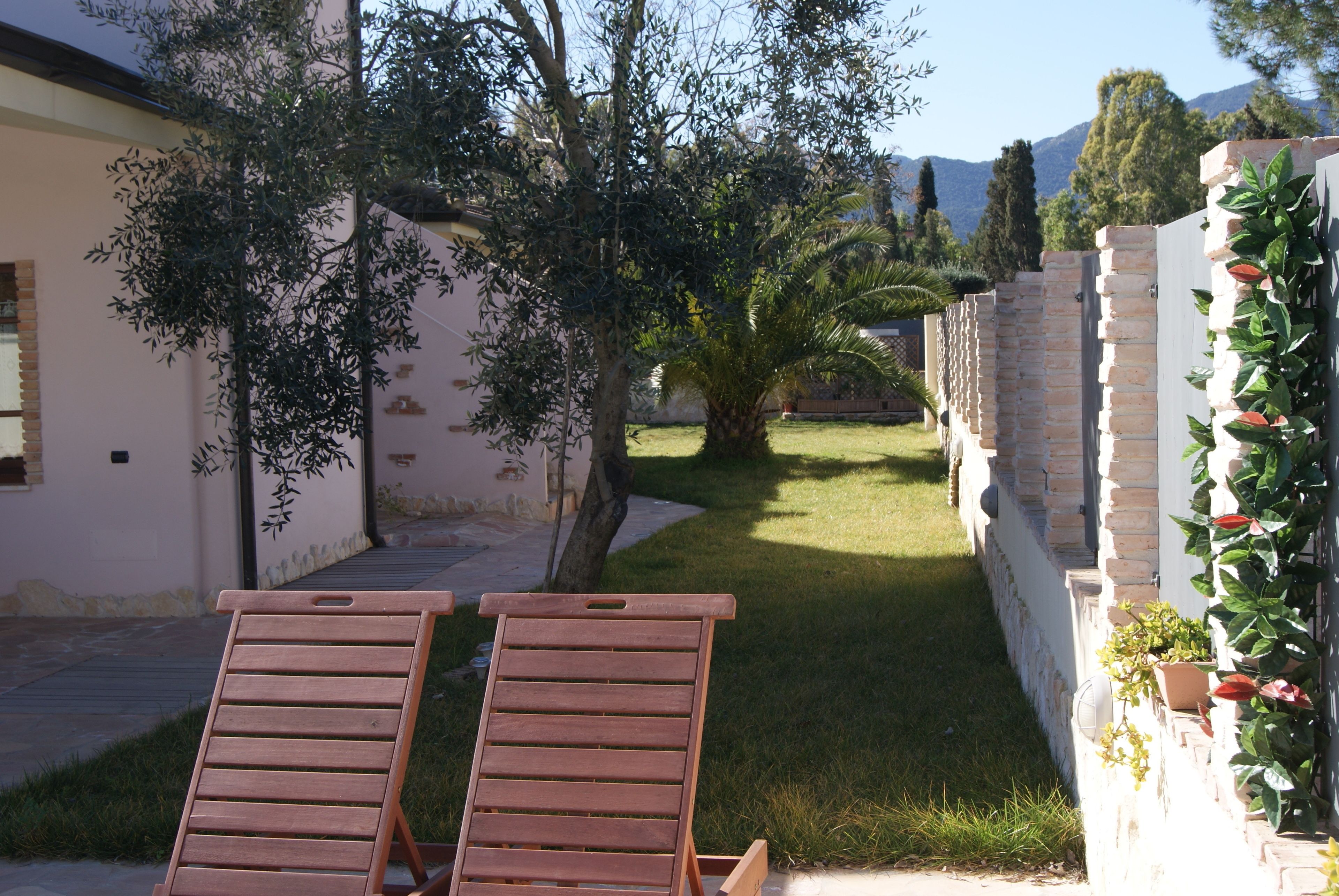 Deux fauteuils de jardin en bois, placés dans un espace aménagé avec un mur en briques et des plantes en pot.