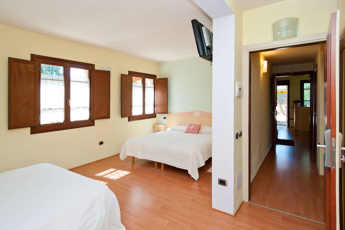 A bedroom with two beds, wooden flooring, and a TV mounted on the wall.