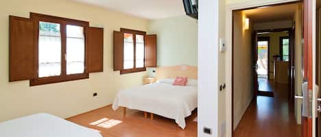 A bedroom with two beds, wooden flooring, and a TV mounted on the wall.