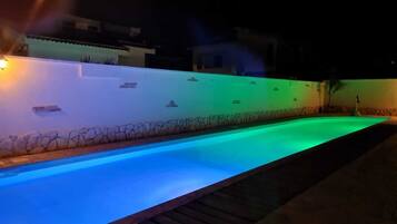 Ein Schwimmbecken bei Nacht mit einer Steinmauer und einer Holzterrasse.