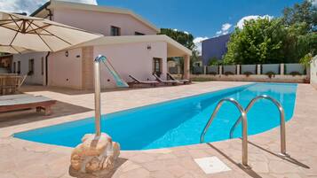 Relax by the pool surrounded by lush greenery and a stone sculpture.