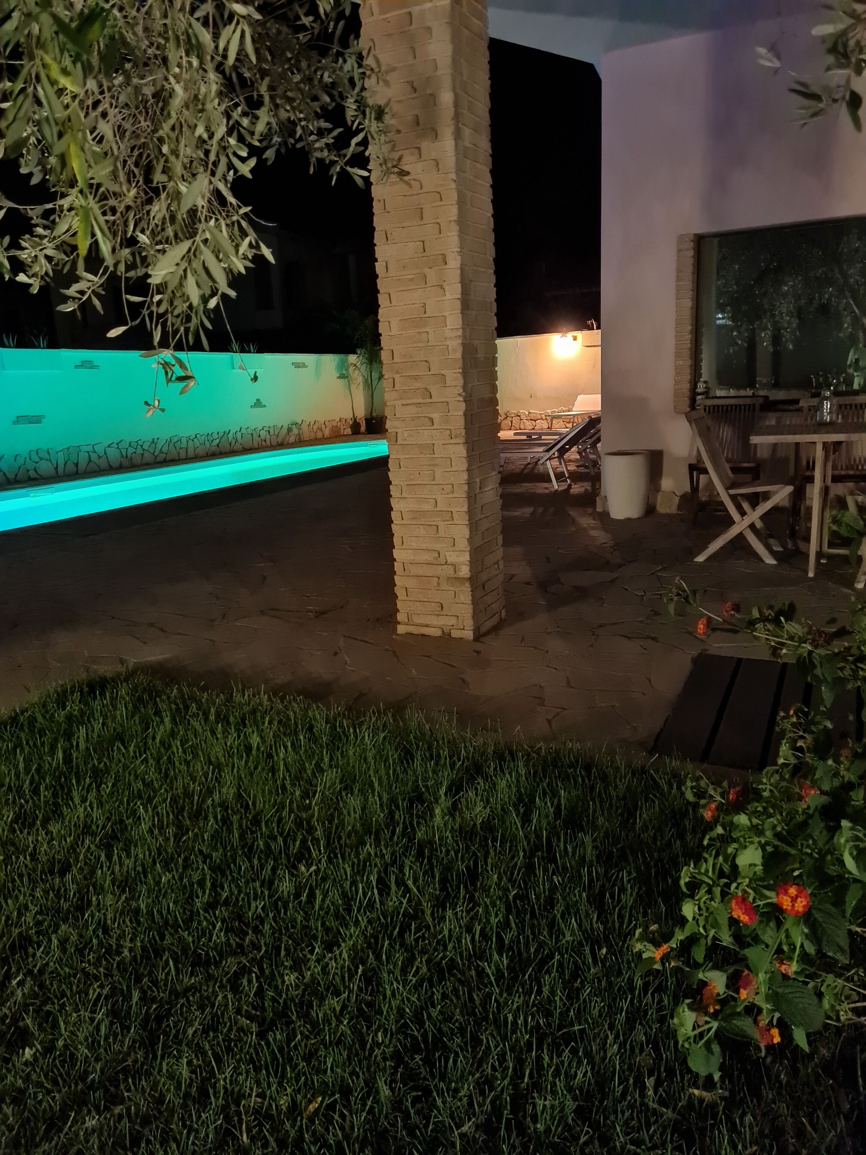 Ein Außenbereich bei Nacht mit Schwimmbad, einem Backsteinpfeiler und einem Tisch mit Stühlen.