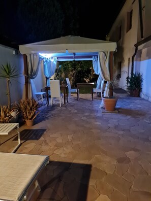 Un patio al aire libre con zona de estar cubierta, suelo de piedra y plantas en macetas.