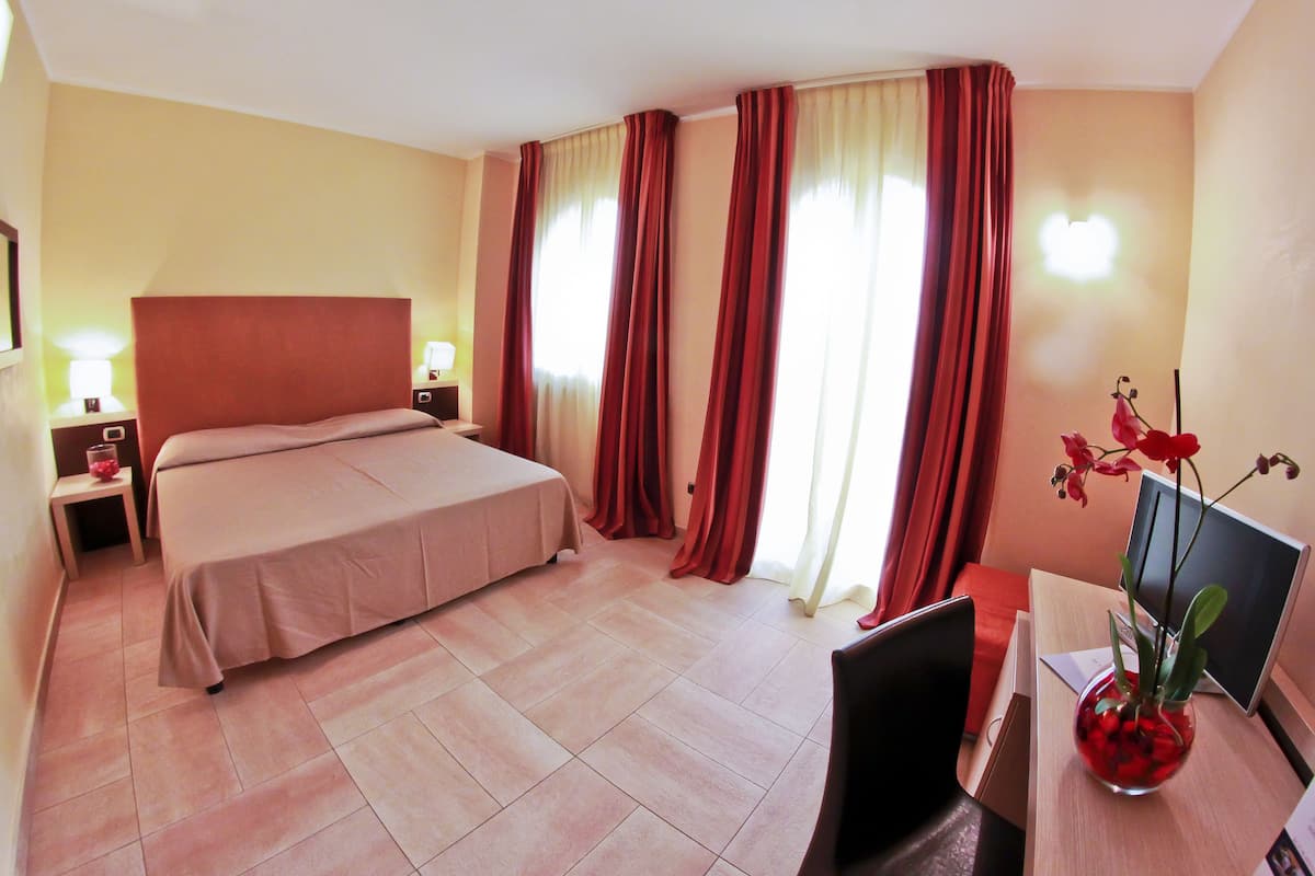 Una habitación de hotel con una cama grande, un escritorio con una computadora y un florero con flores.