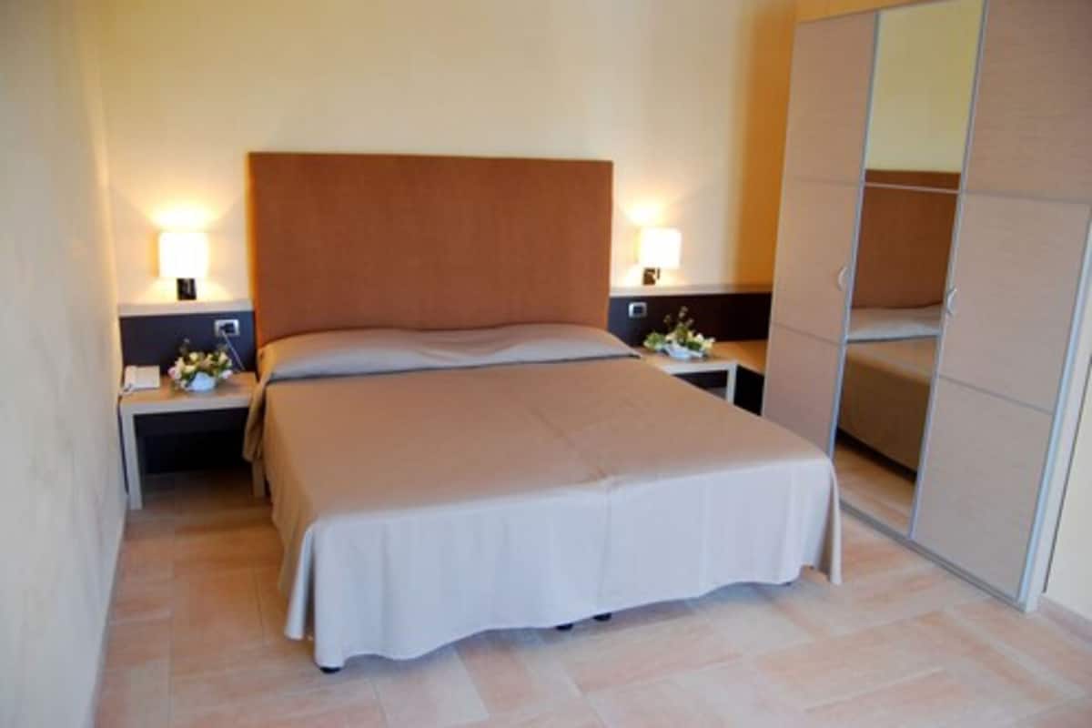 Una habitación de hotel con una cama grande, dos mesitas de noche con lámparas y un armario.
