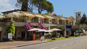 A two-story building with outdoor seating, a restaurant sign, and a clock tower. - Hotel Aquavite (Gardone Riviera)
