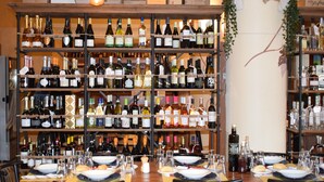A restaurant with multiple tables set for dining, surrounded by shelves of wine bottles. - Hotel Aquavite (Gardone Riviera)