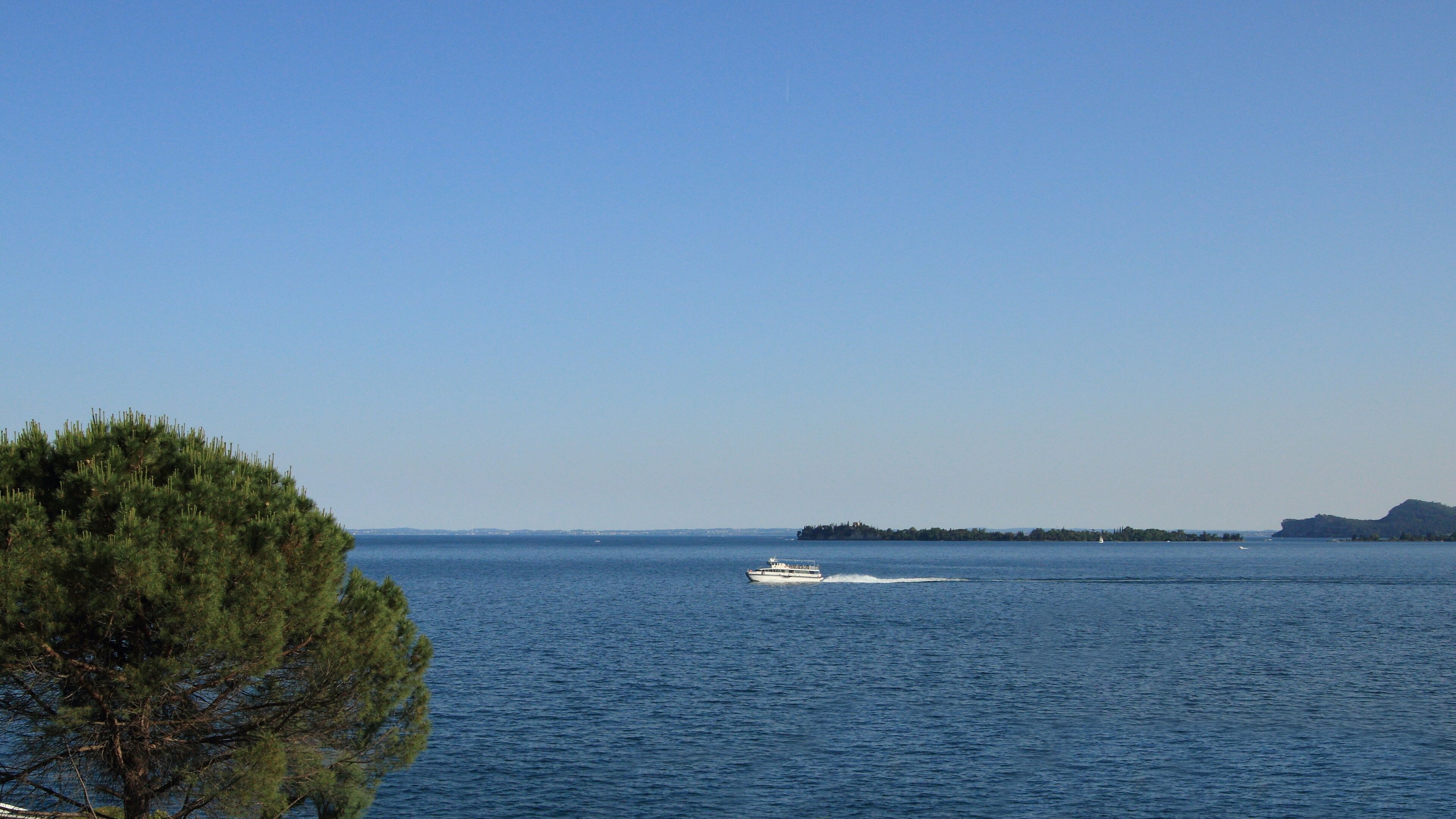 A clear view of a body of water with a boat in motion, surrounded by a coastline with dense greenery and a distant island.