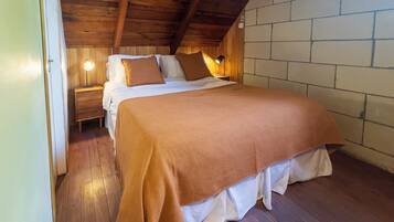 A cozy bedroom with a wooden ceiling, a brick wall, and a bed with a brown blanket.