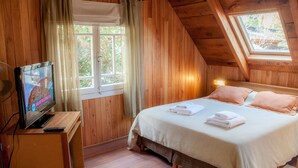 A cozy wooden room with a bed, a TV on a stand, and a window with curtains.
