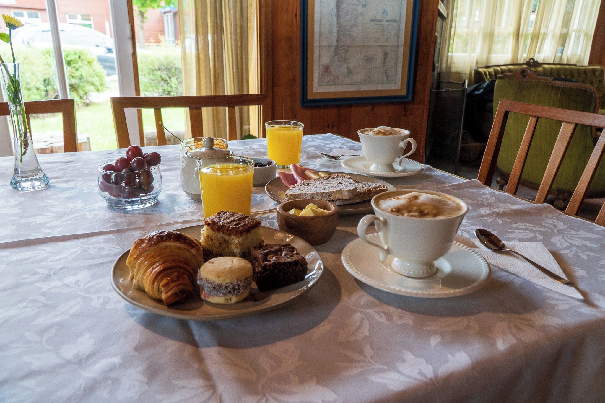 Una mesa de desayuno con cruasanes, scones y un bol de fruta.