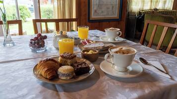 Una mesa de desayuno con cruasanes, scones y un bol de fruta.