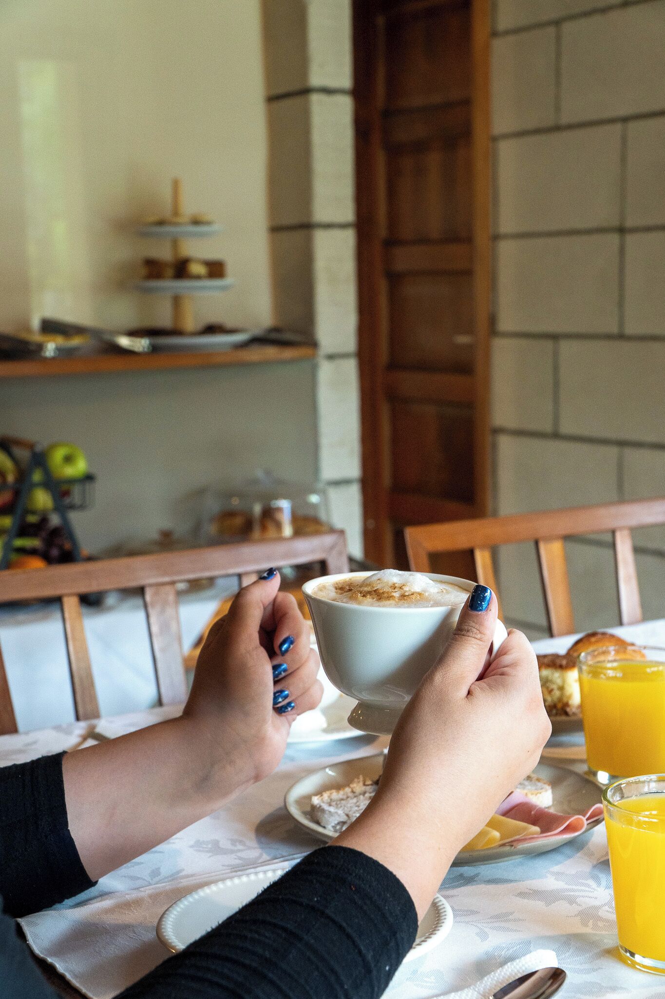 Uma pessoa segurando uma xícara de café em uma mesa com itens de café da manhã e um copo de suco de laranja.