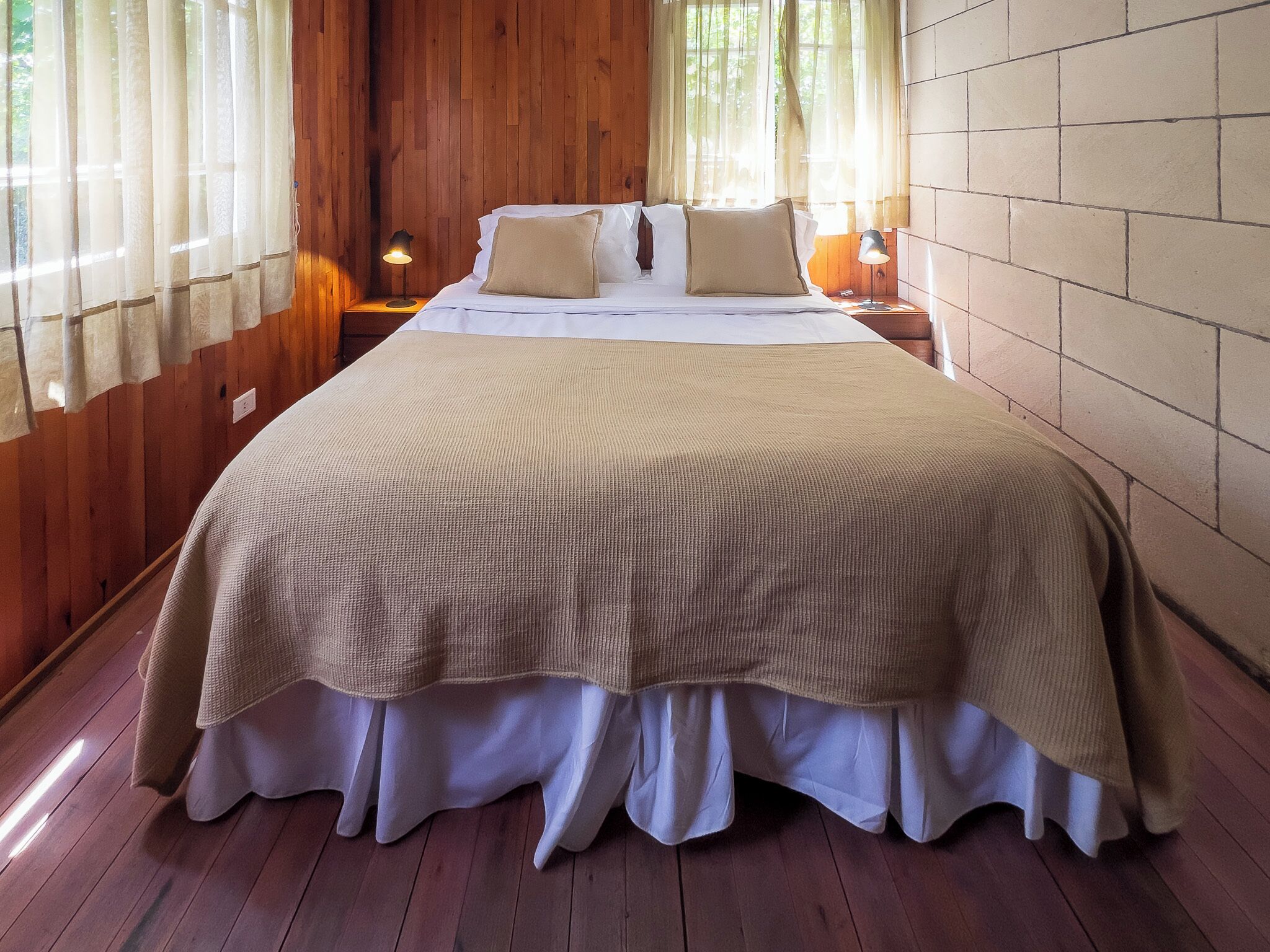 Een kamer met houten lambrisering, een groot bed, witte beddengoed en twee bedlampjes.