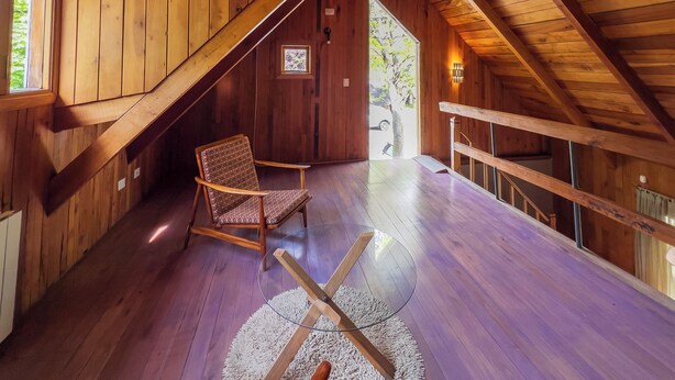 A wooden interior with a sloped ceiling, a chair, a small table, and a view through a door.