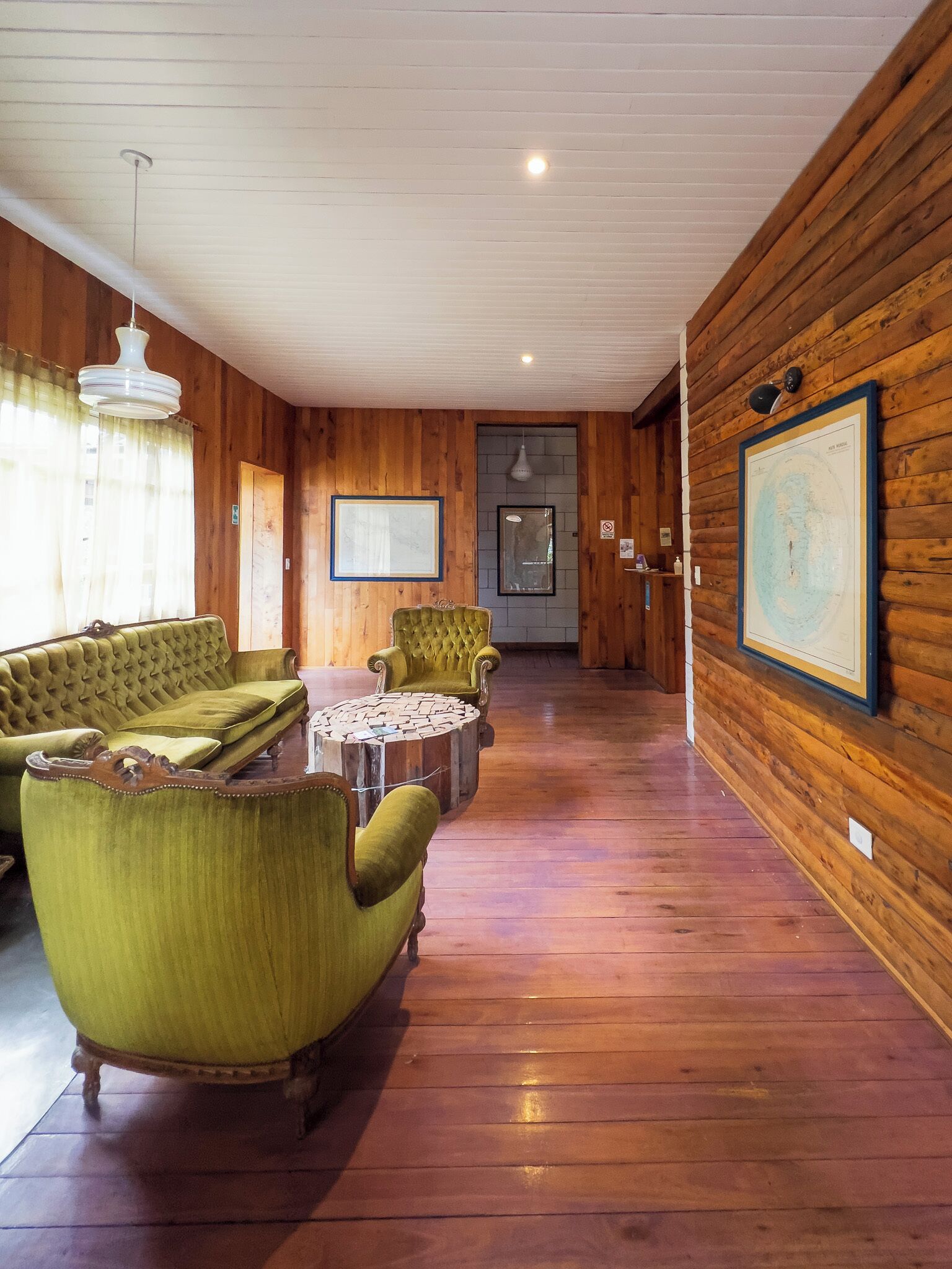 Une pièce avec des boiseries, un canapé vert, un fauteuil vert, une table basse ronde et une carte encadrée accrochée au mur.