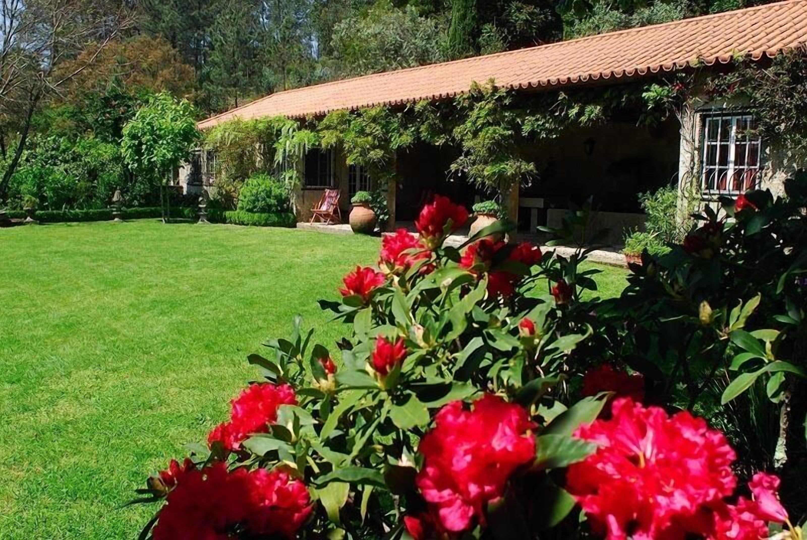 Una casa con techo de tejas, rodeada de un césped cuidado y plantas en flor.