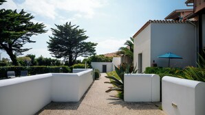 A pathway flanked by white walls and greenery, leading to a building with a blue umbrella.