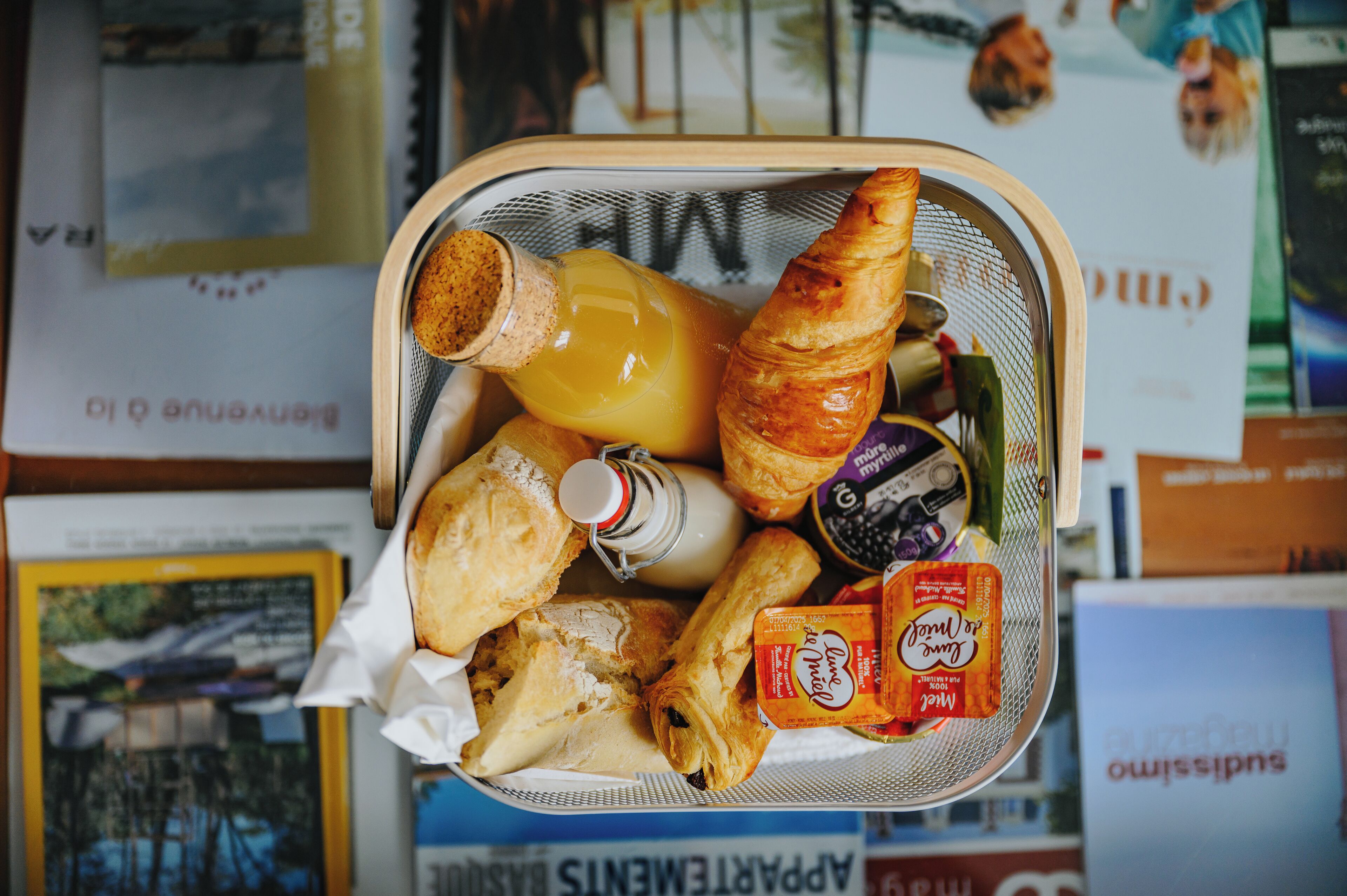 A basket containing a croissant, a bottle of orange juice, a pastry, and a small container of jam.