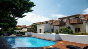 A swimming pool with wooden deck and lounge chairs, surrounded by white walls and balconies.