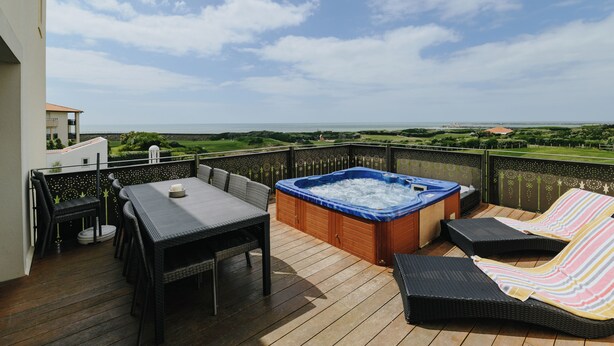 A balcony with a hot tub, lounge chairs, and a dining table.