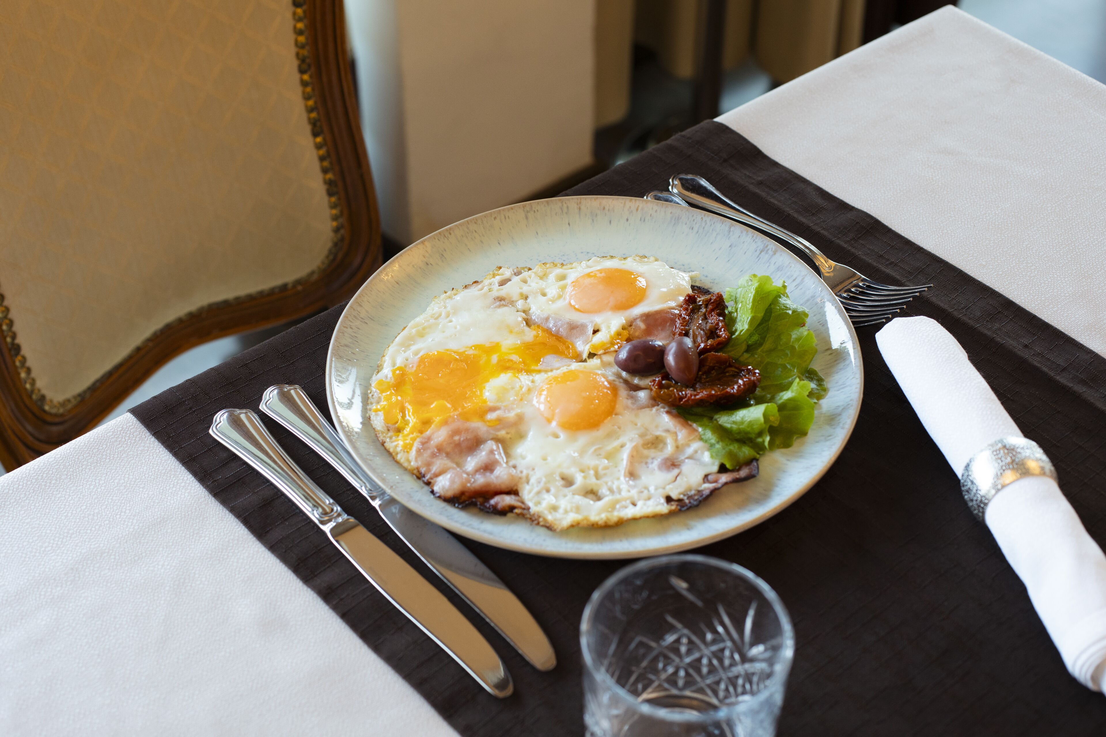 A plate of eggs, bacon, and greens on a table with cutlery and a napkin.