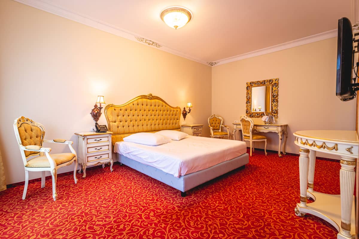 Habitación de hotel con una cama grande, un escritorio, una silla, un aparador y un espejo.