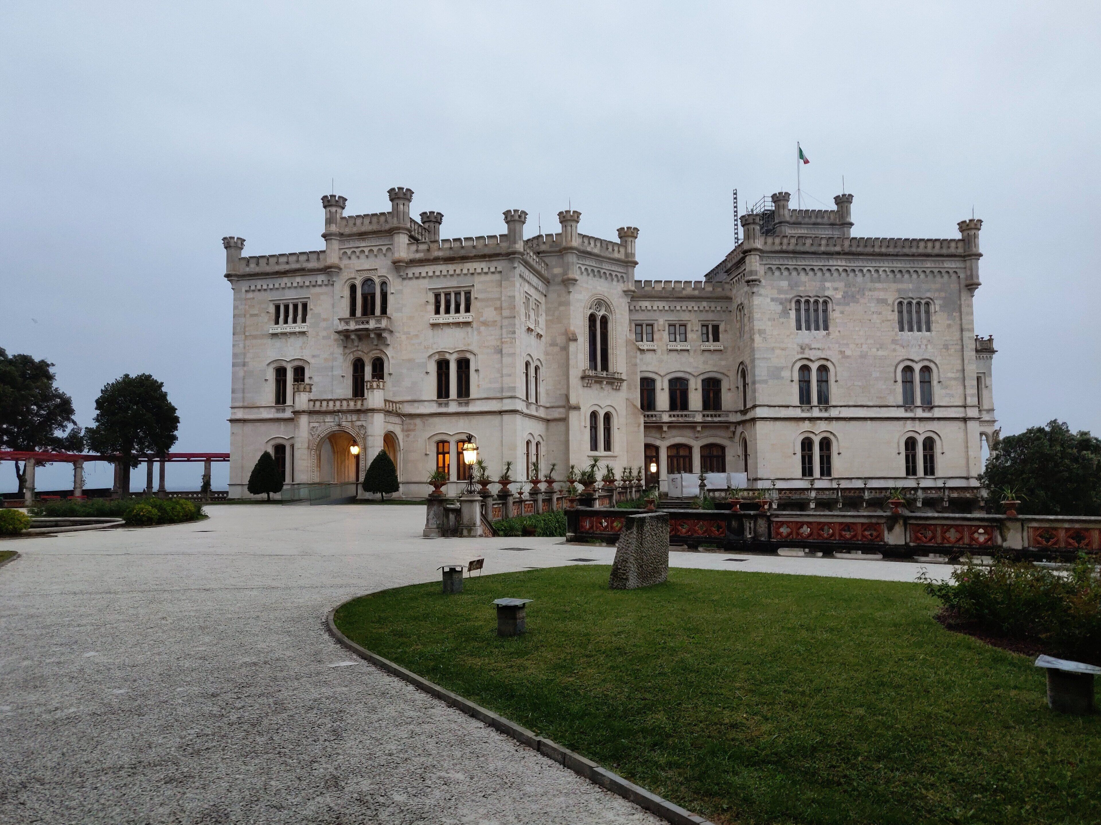 A large, historic building with a symmetrical facade, multiple windows, and a flag on top.
